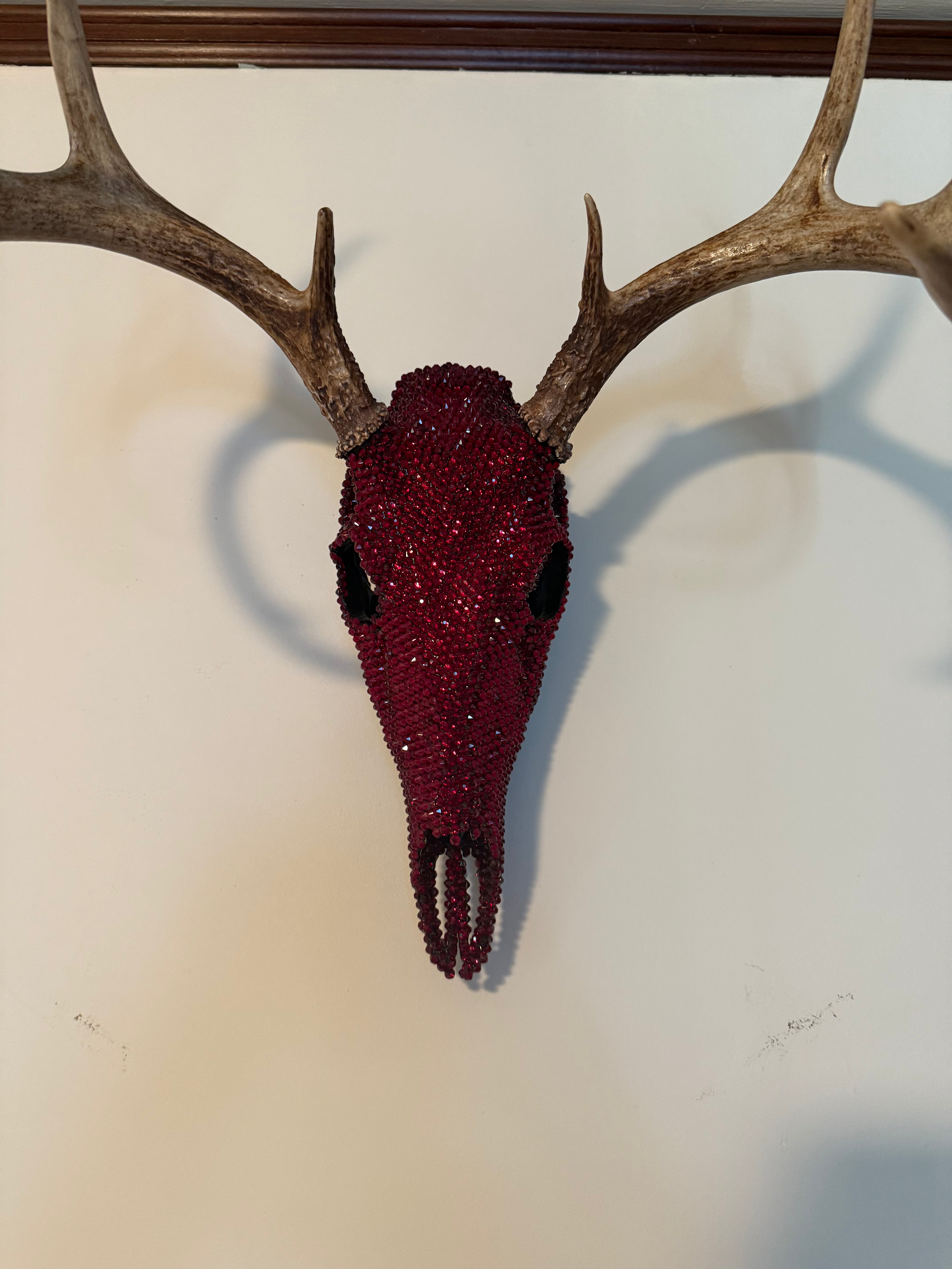Crimson Autumn - eight-point buck skull hand-set with thousands of dark siam red glass rhinestones, hung on a white wall